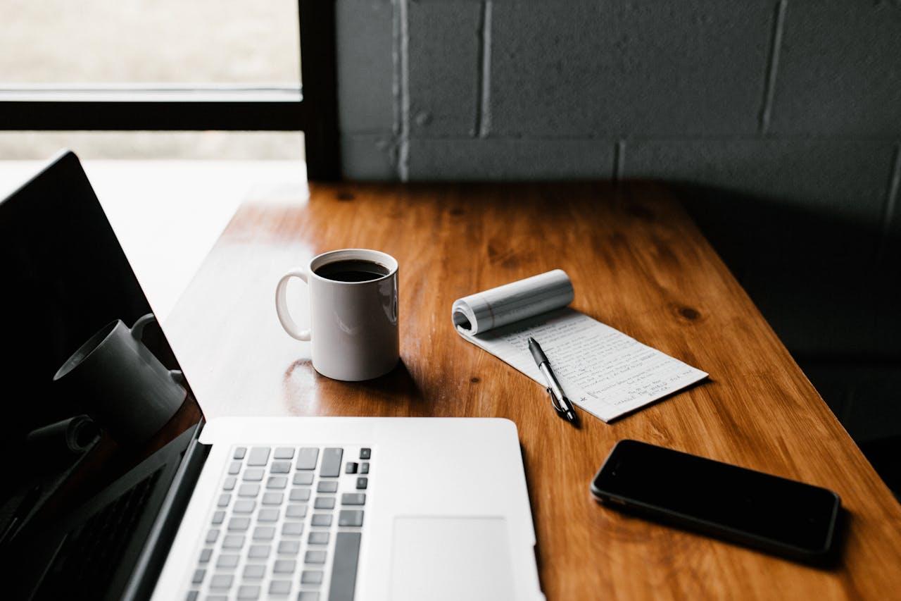 Produktiver Start in den Tag mit Kaffee, Notizblock und Laptop.