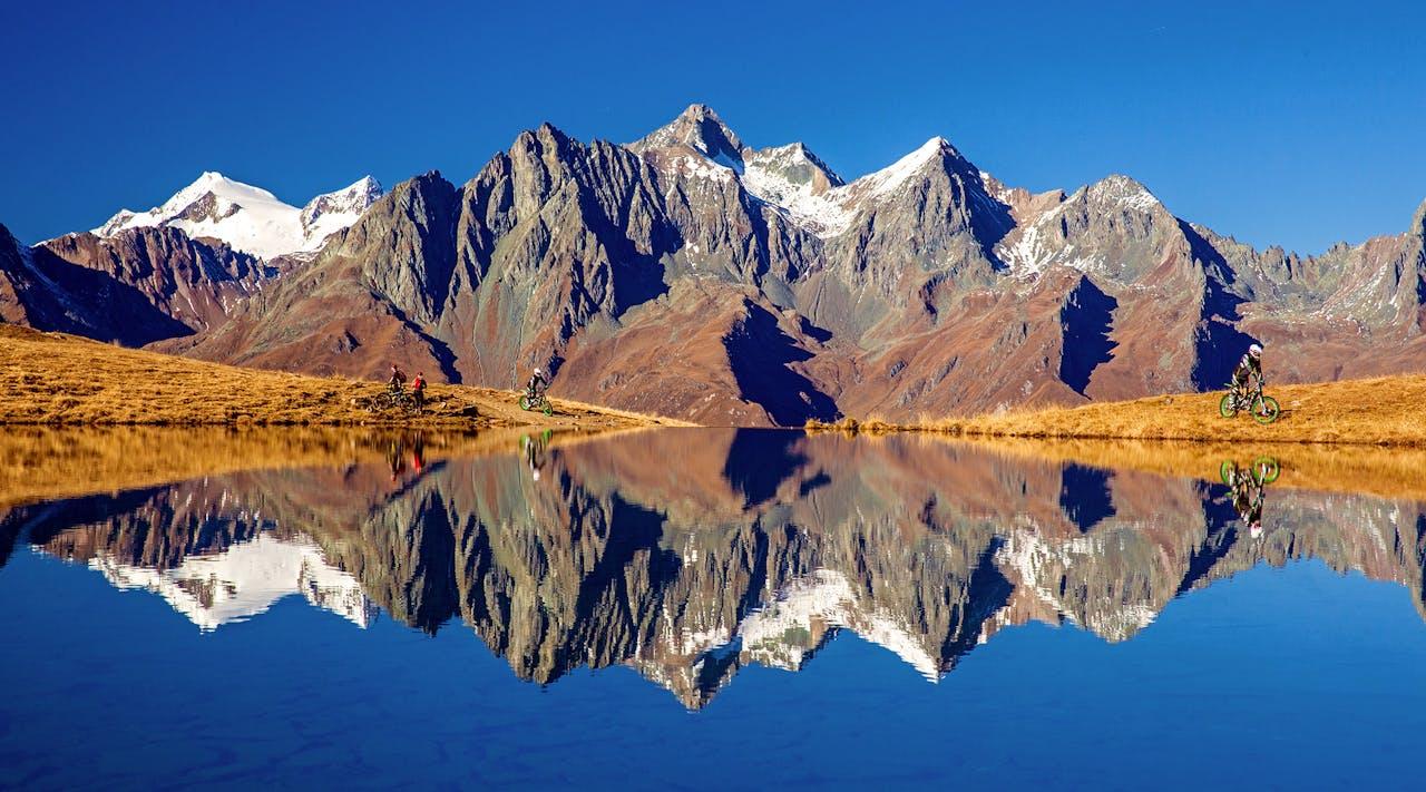 Berge, Spiegelsee, Radfahrer, klarer Himmel.